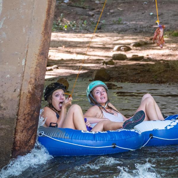 Tubers grab bacon dangling from string on poles from the 9th Street bridge during the 2019 Tube to Work Day down Boulder Creek.