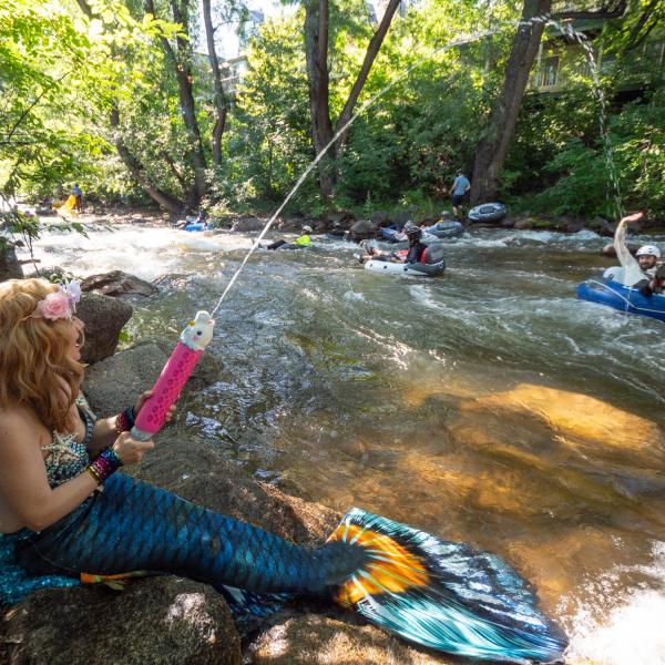 A woman dressed in a mermaid costume uses a soaker on participants in the 2019 Tube to Work Day along Boulder Creek.
