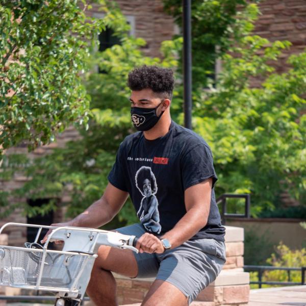 A masked student rides a bike on the CU Boulder campus during the first week of classes. (Photo by Glenn Asakawa/University of Colorado)