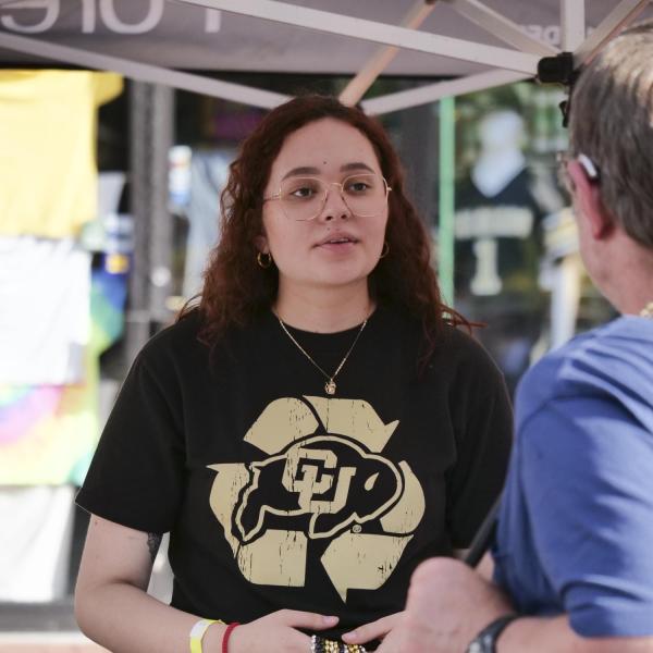 Volunteer speaks with visitors at a CU table on Pearl Street