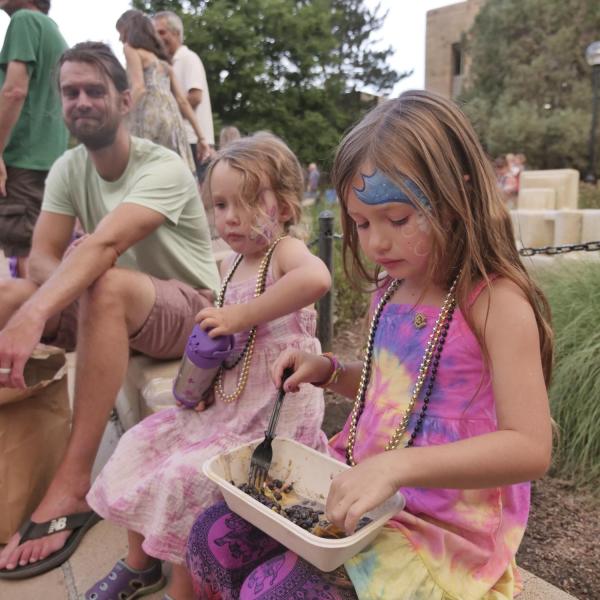Kids with their faces painted sit on a curb to eat during Bands on the Bricks
