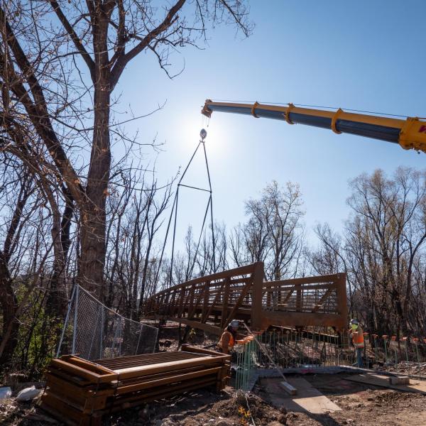 Workers use a mobile crane to place a 33-ton bridge over Boulder Creek on East Campus. Photo by Glenn Asakawa.