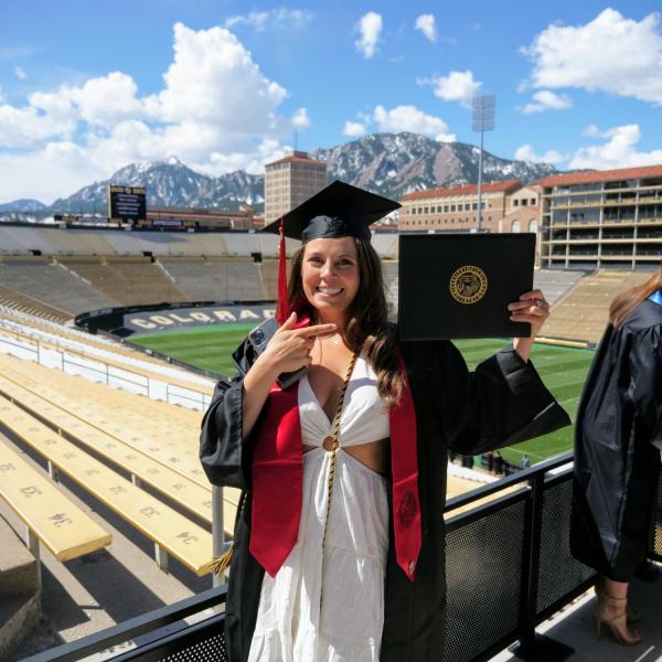 Journalism graduate Kiely Weshoff points to her diploma board after getting her photo taken in Folsom Field during CU Boulder’s Graduate Appreciation Days events on April 23, 2021. (Photo by Glenn Asakawa/University of Colorado)