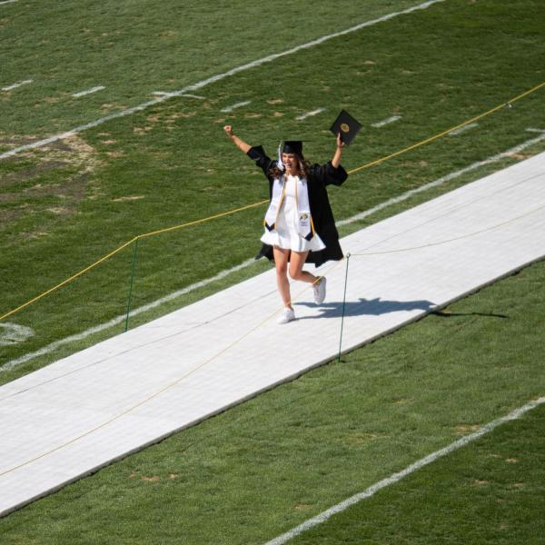 A graduate celebrates after getting her photo taken at Folsom Field during CU Boulder’s Graduate Appreciation Days events. (Photo by Glenn Asakawa/University of Colorado)