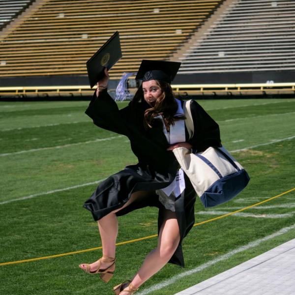 Katie Burns kicks up her heels after getting her photo taken at Folsom Field during CU Boulder’s Graduate Appreciation Days. (Photo by Glenn Asakawa/University of Colorado)