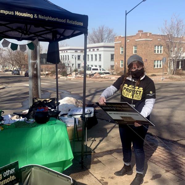 A person at a Campus Housing & Neighborhood Relations booth in a Protect Our Herd T-shirt.
