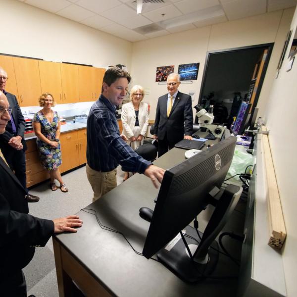 Joe Dragabon, director of Biofrontiers Advanced Light Microscope Core, demonstrates research conducted with the technology for CU President Mark Kennedy, far right, as others, including CU Boulder Chancellor Phil DiStefano, left, listen. (Photo by Glenn Asakawa/University of Colorado)