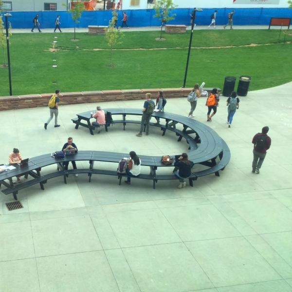 Several people sit at a question-mark-shaped picnic table at the VAC