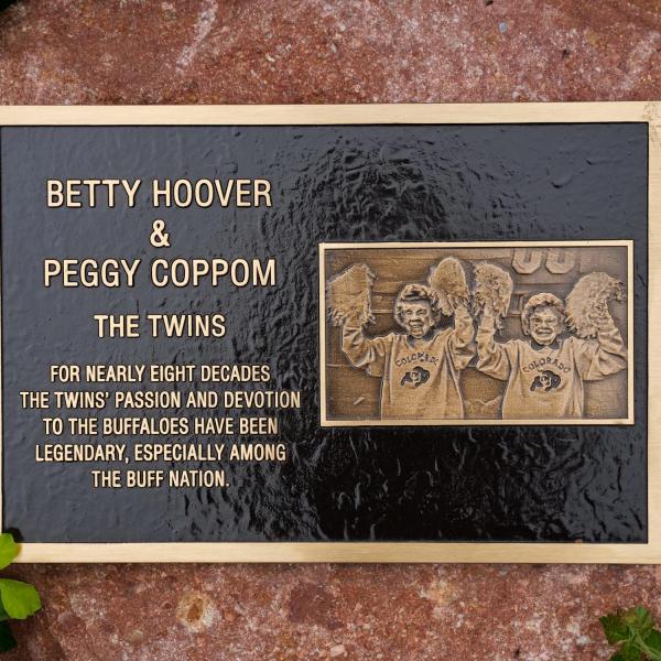 A plaque honoring the late Betty Hoover and her twins sister, Peggy Coppom, sits between "twin" trees planted along the Buff Walk on the east side of Folsom Field. (Photo by Glenn Asakawa/University of Colorado)