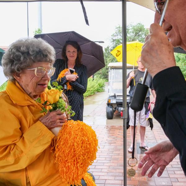 Chancellor Philip DiStefano presents Peggy Coppom with a vase with two yellow roses after he, Athletic Director Rick George and others gathered on Saturday, June 26, for a tree dedication ceremony honoring Coppom and her late sister Betty Hoover. (Photo by Glenn Asakawa/University of Colorado)