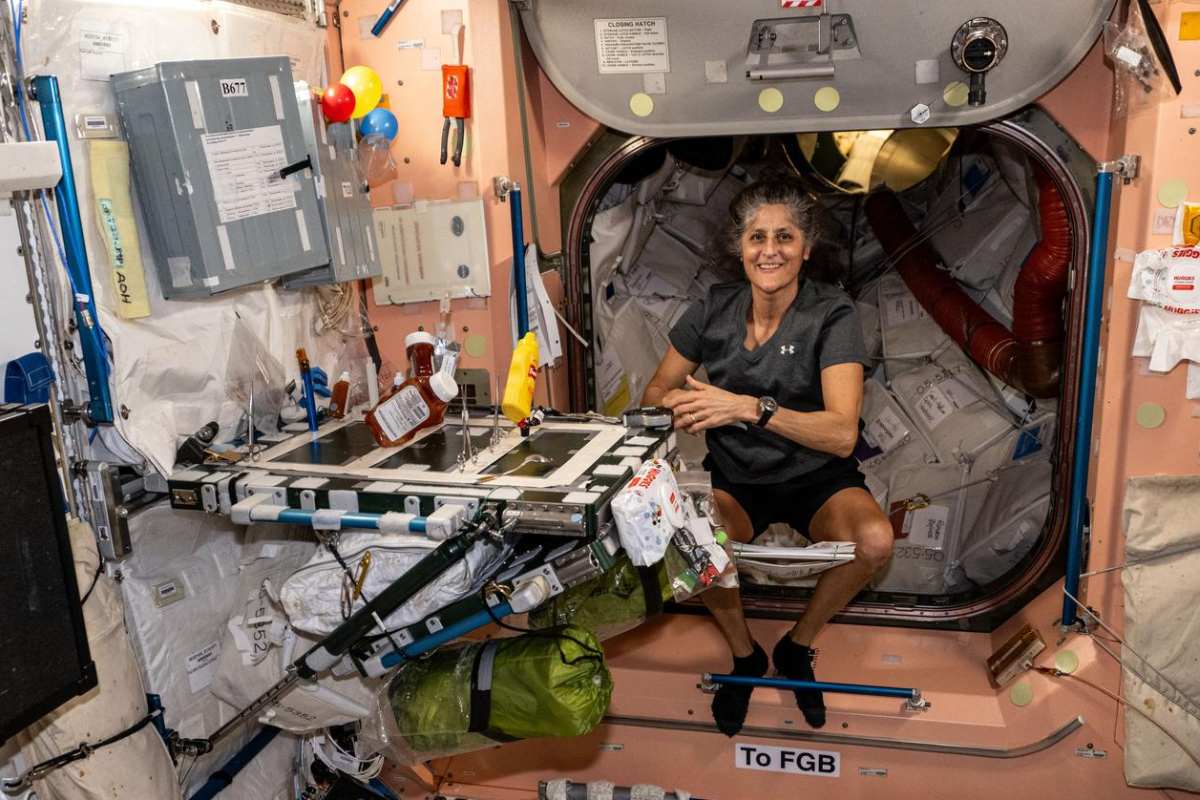 Woman wearing a t-shirt and shorts seated in a cluttered cabin aboard a space station