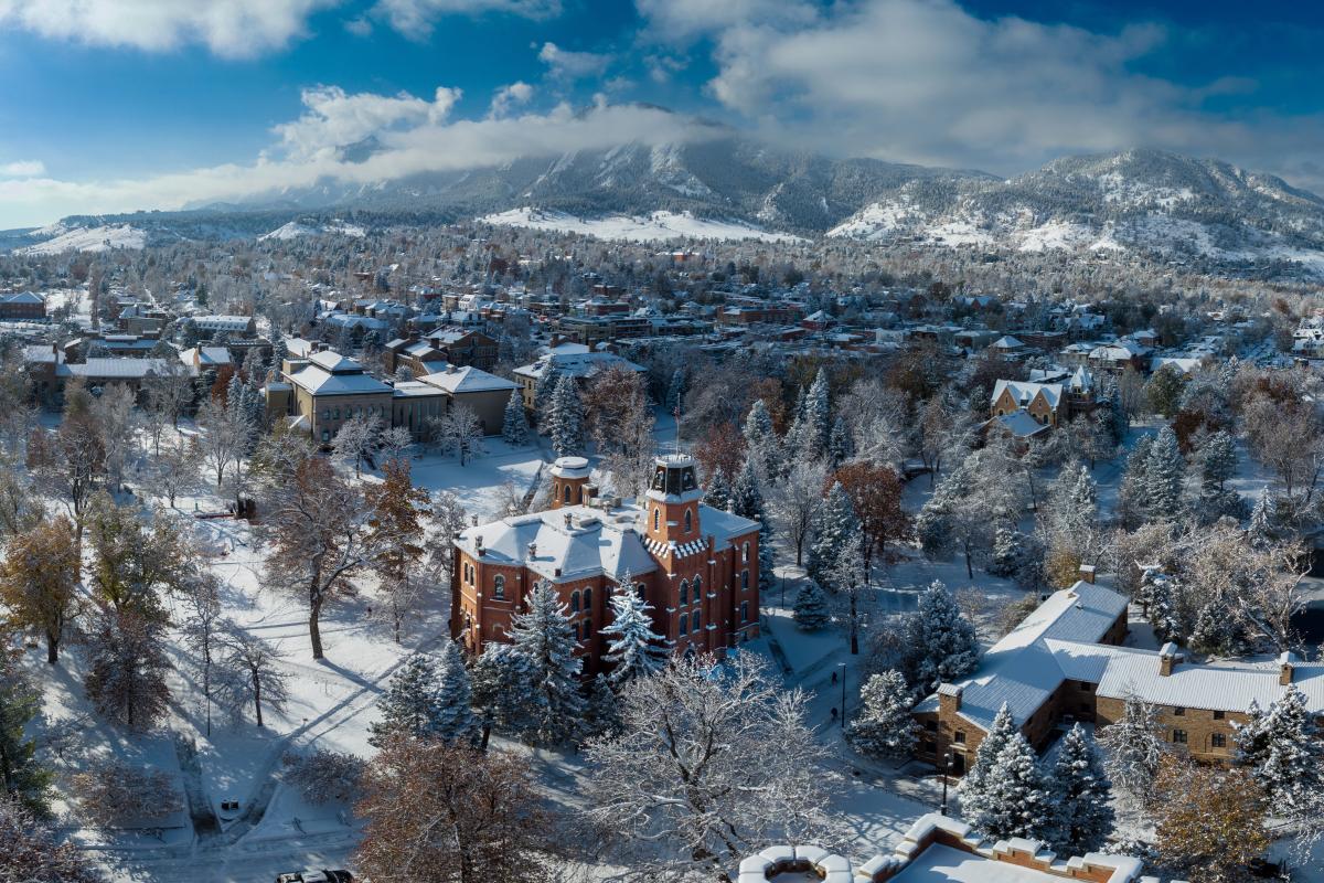 Drone shot of Old Main with the Flatirons in the background on a snowy day