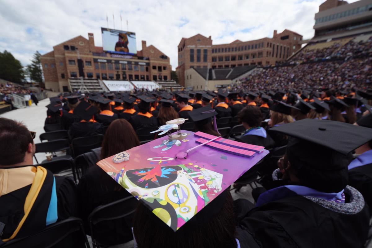 Graduates sit on Folsom Field during commencement ceremony