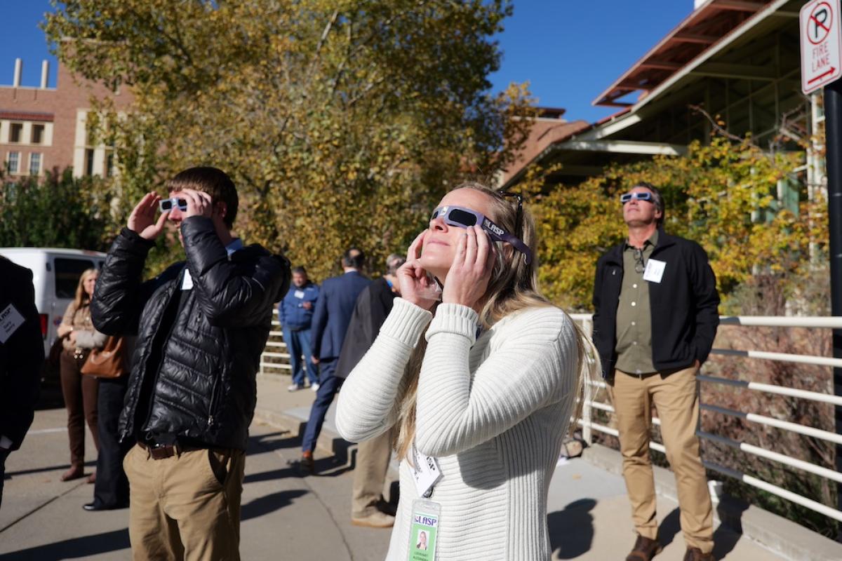 People wearing protective glasses look up at the sky