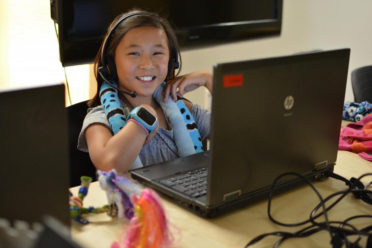 A student sits at a computer smiling