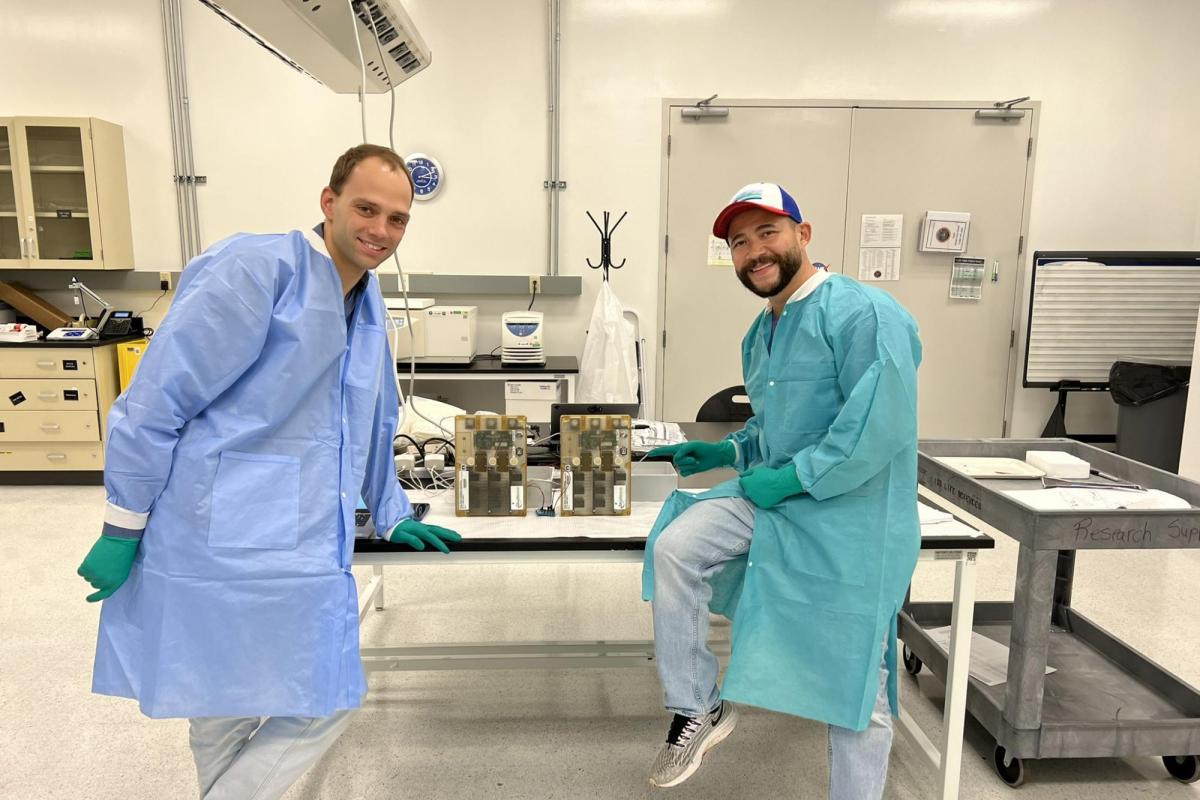 Tobias Niederwieser and Luis Zea pose by two cases on a table in a lab