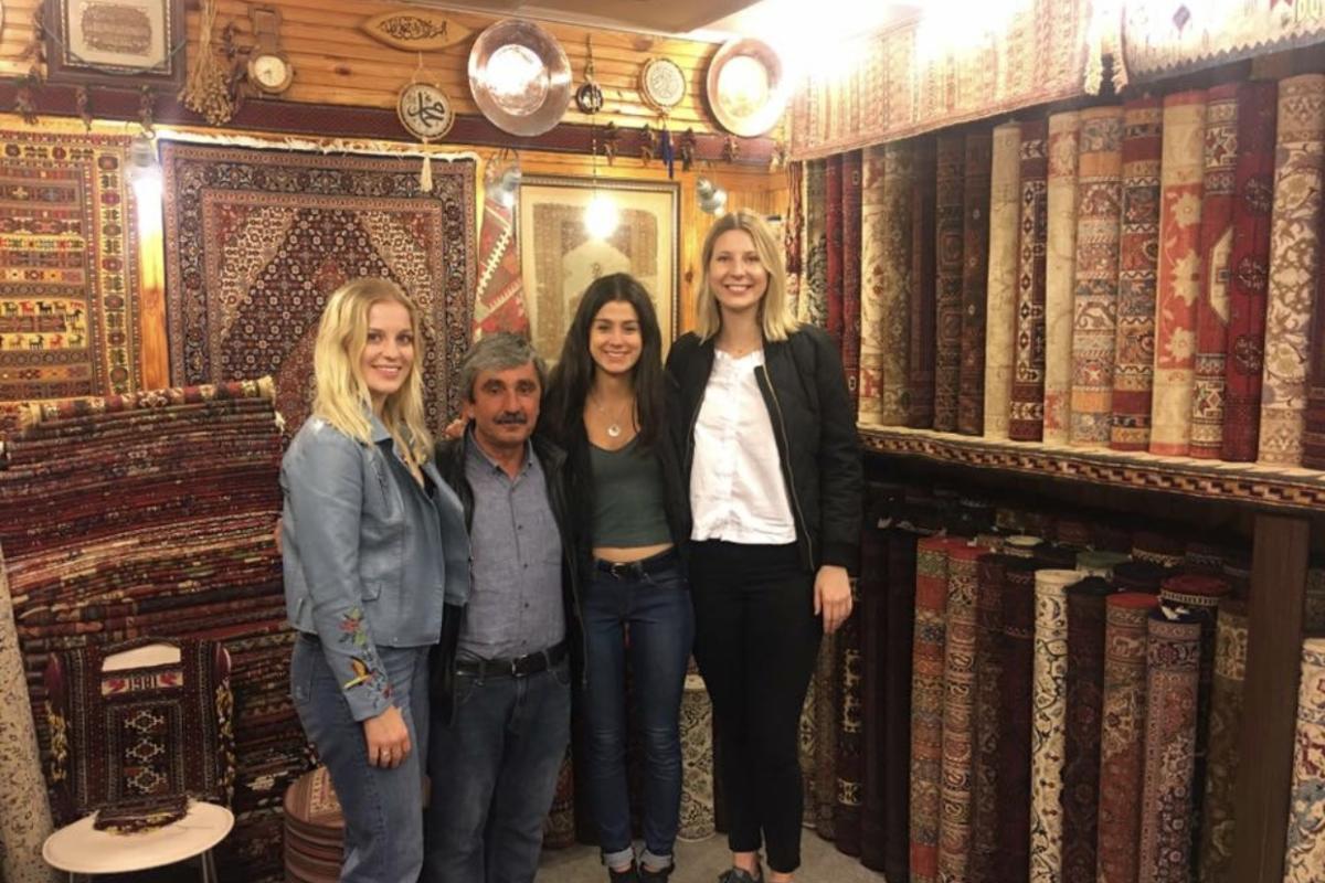 Three female college students pose with owner of carpet shop in Istanbul, Turkey
