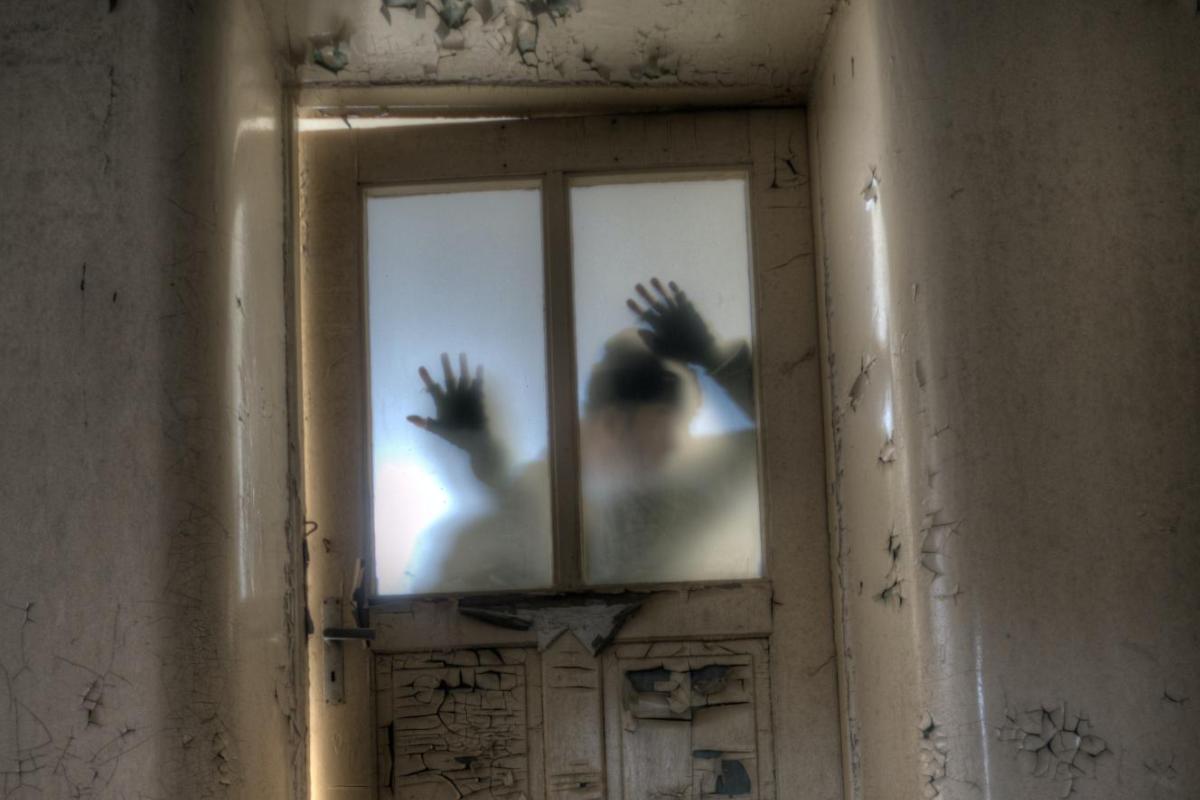 Sillhouette of hands pressed against a window in an old building