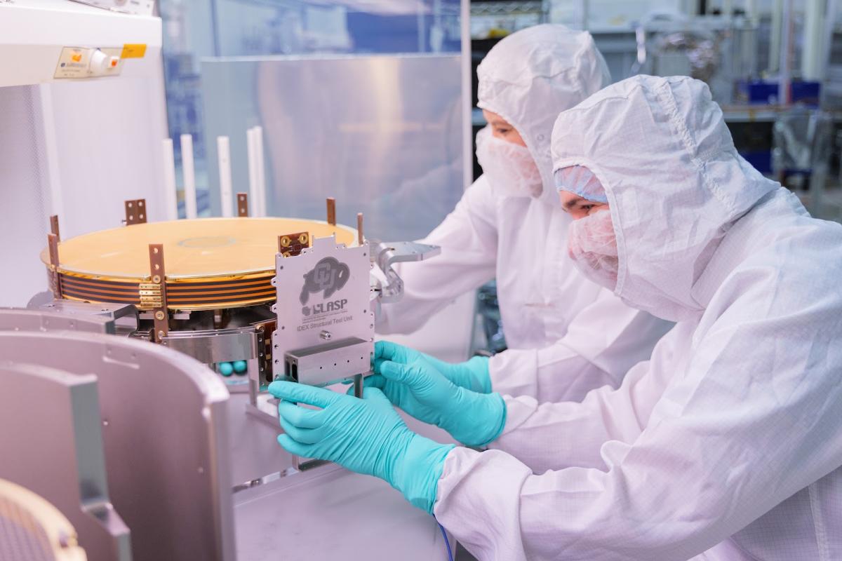 People in protective suits place a plaque on a space instrument in a clean room
