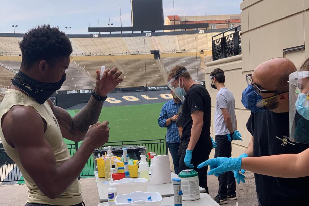 CU Boulder athlete holds up a vial for testing his saliva for the coronavirus.