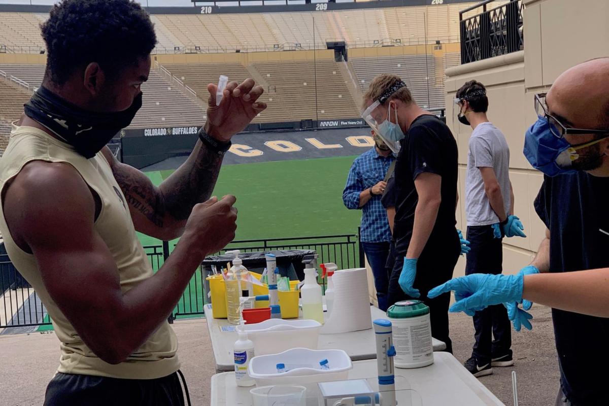 CU Boulder athlete holds up a vial for testing his saliva for the coronavirus.