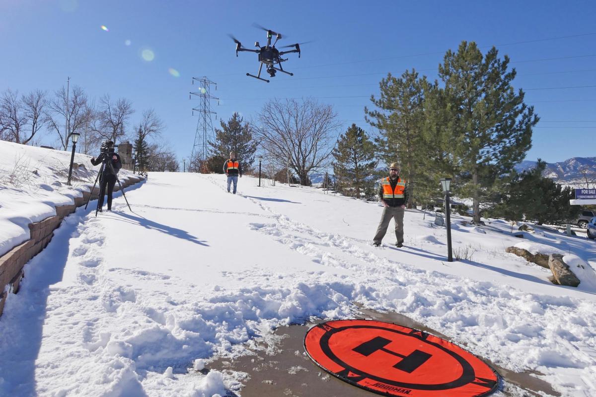 Members of the GEER team watch a drone take off from a snowy driveway