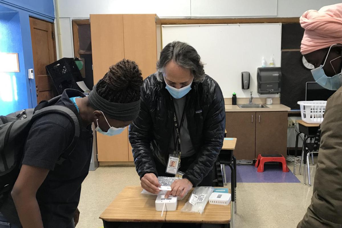 Professor Mark Hernandez demonstrates the installation process for the classroom air quality remote sensors to CU Boulder student volunteer technicians Christiane Nitcheu and Sylvia Akol.