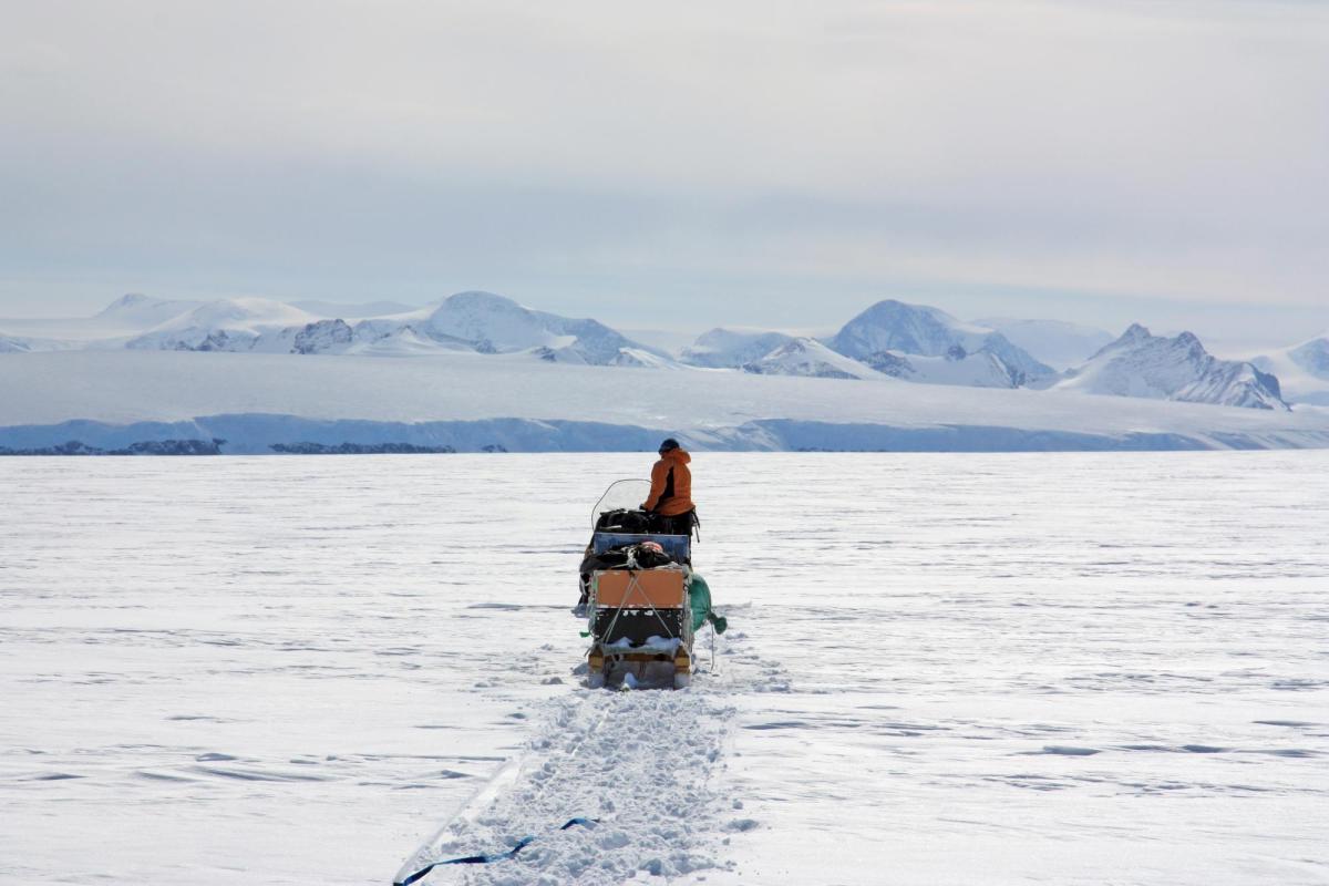 Researcher on a small boat driving toward an ice shelf in Antarctica