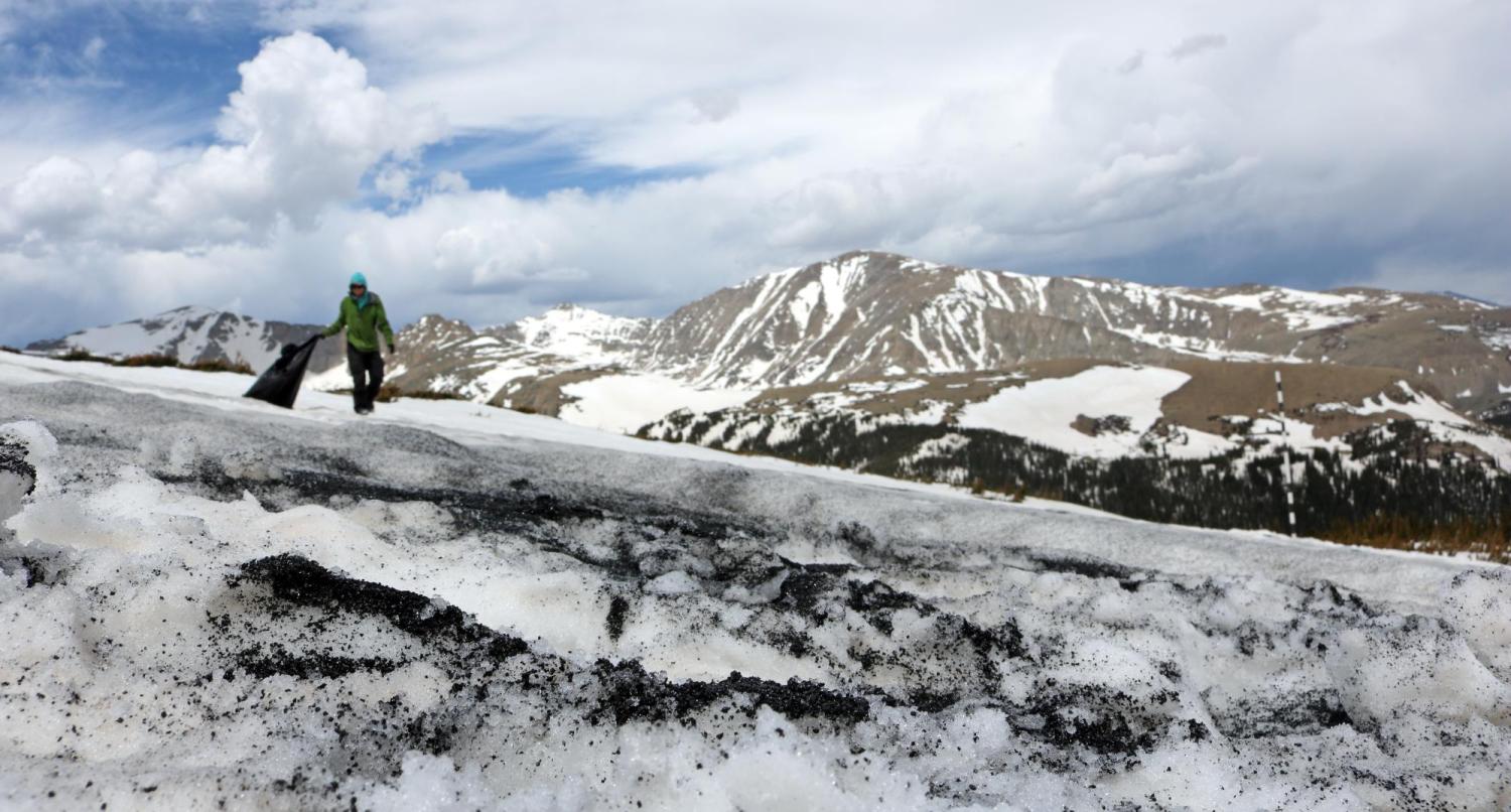  Samuel Yevak carries bags of black sand to where he will apply it on top of the snowpack