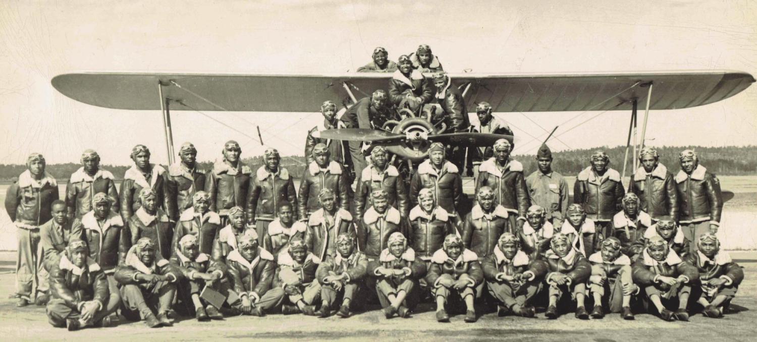 Members of a class of Tuskegee Airmen pose in front of and on an airplane.