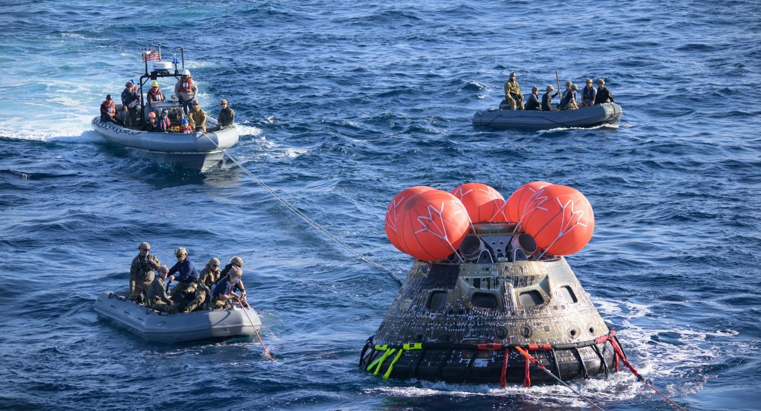 Spacecraft floats in the ocean as several boats packed with people arroach