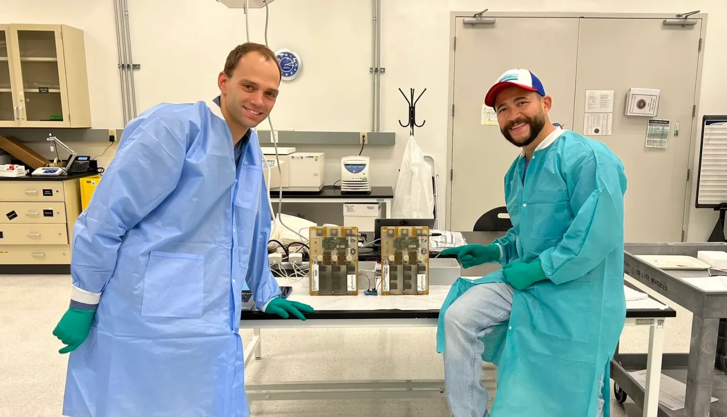 Tobias Niederwieser and Luis Zea pose by two cases on a table in a lab