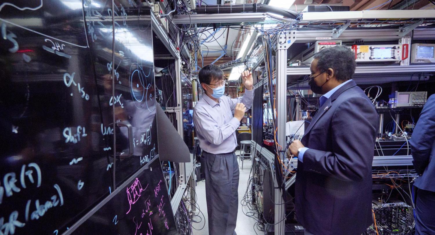 Jun Ye and Joe Neguse in a lab surrounded by machinery
