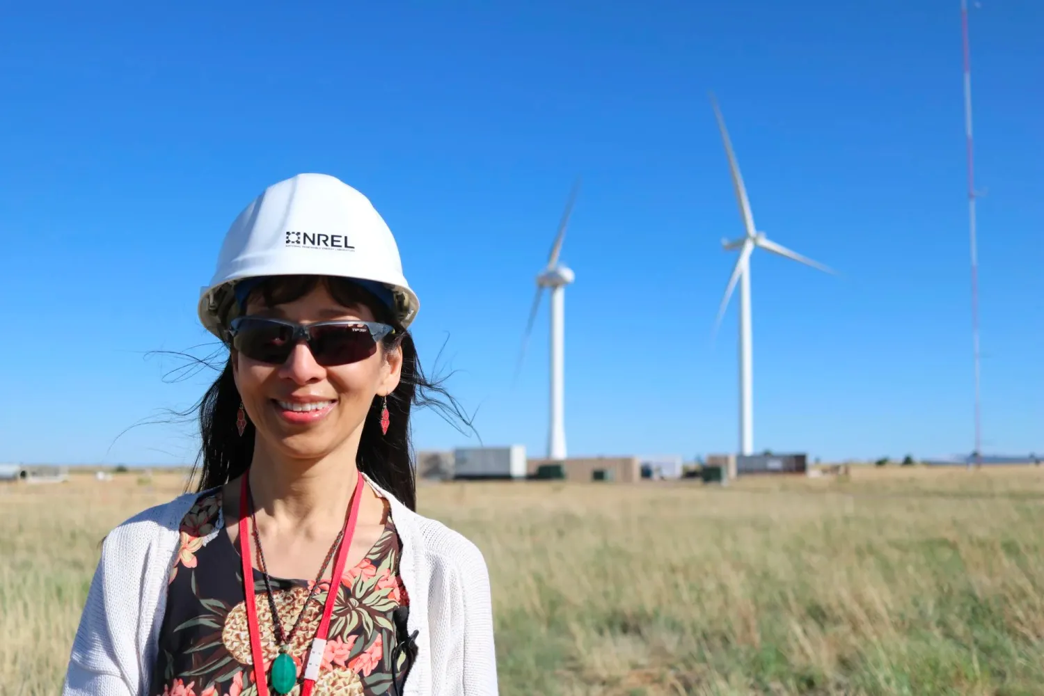 Lucy Pao in a hard hat poses in front of two wind turbines