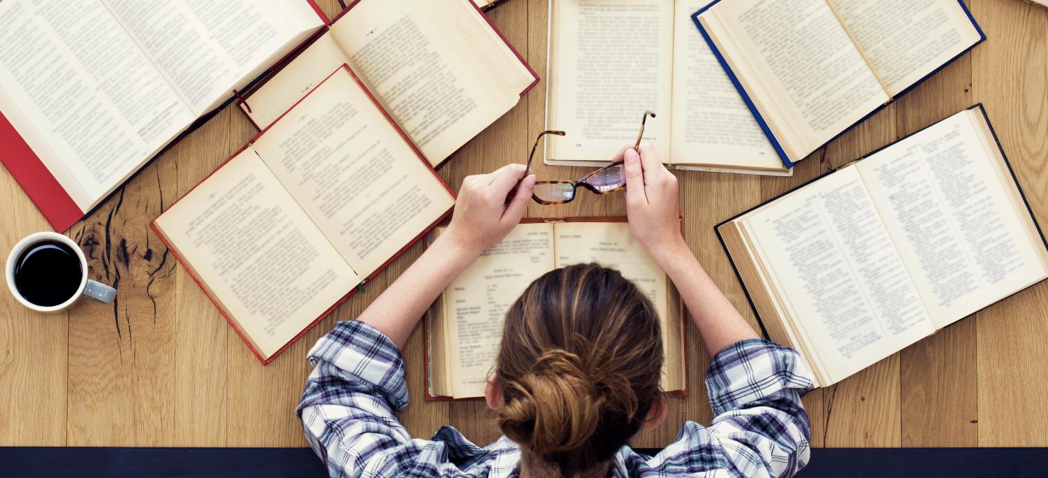 Woman seen from above looks down at books strewn across a table