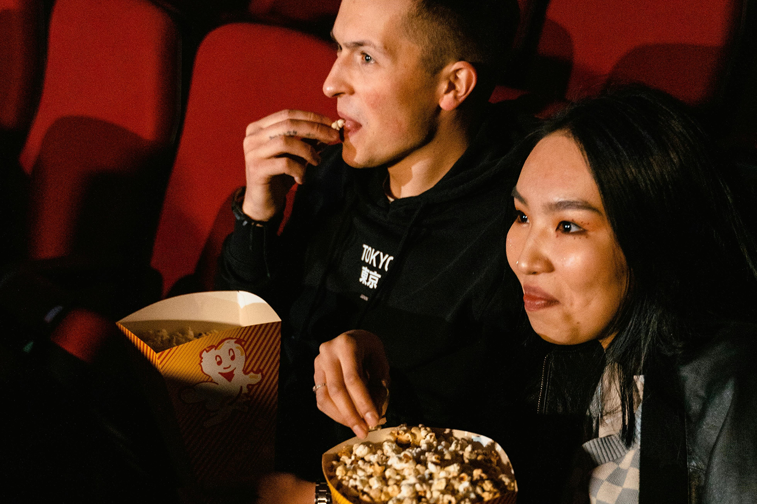 Man and woman sit in theater seats eating popcorn
