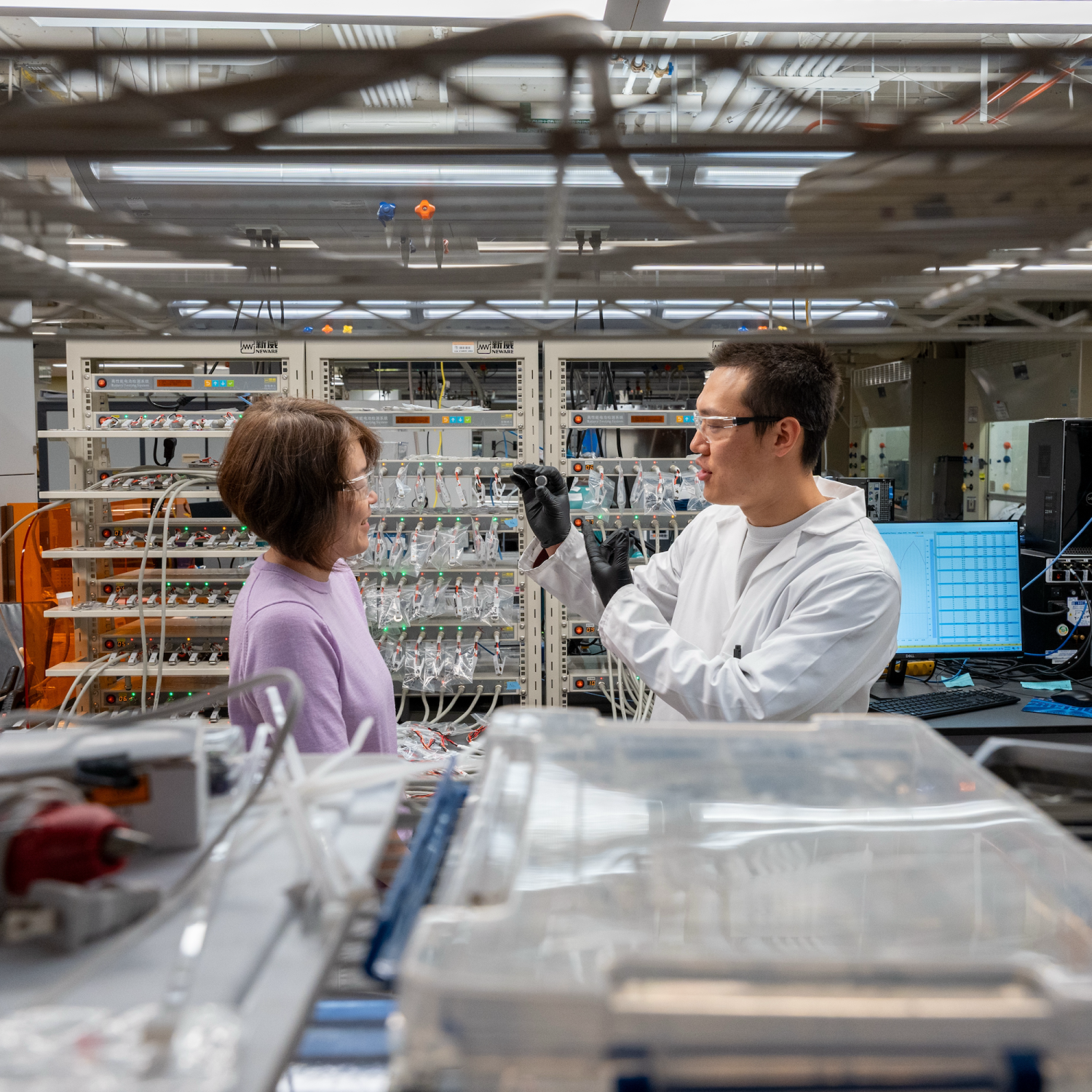 A man and a woman talk to each other in a lab setting amid shelves filled with scientific equipment