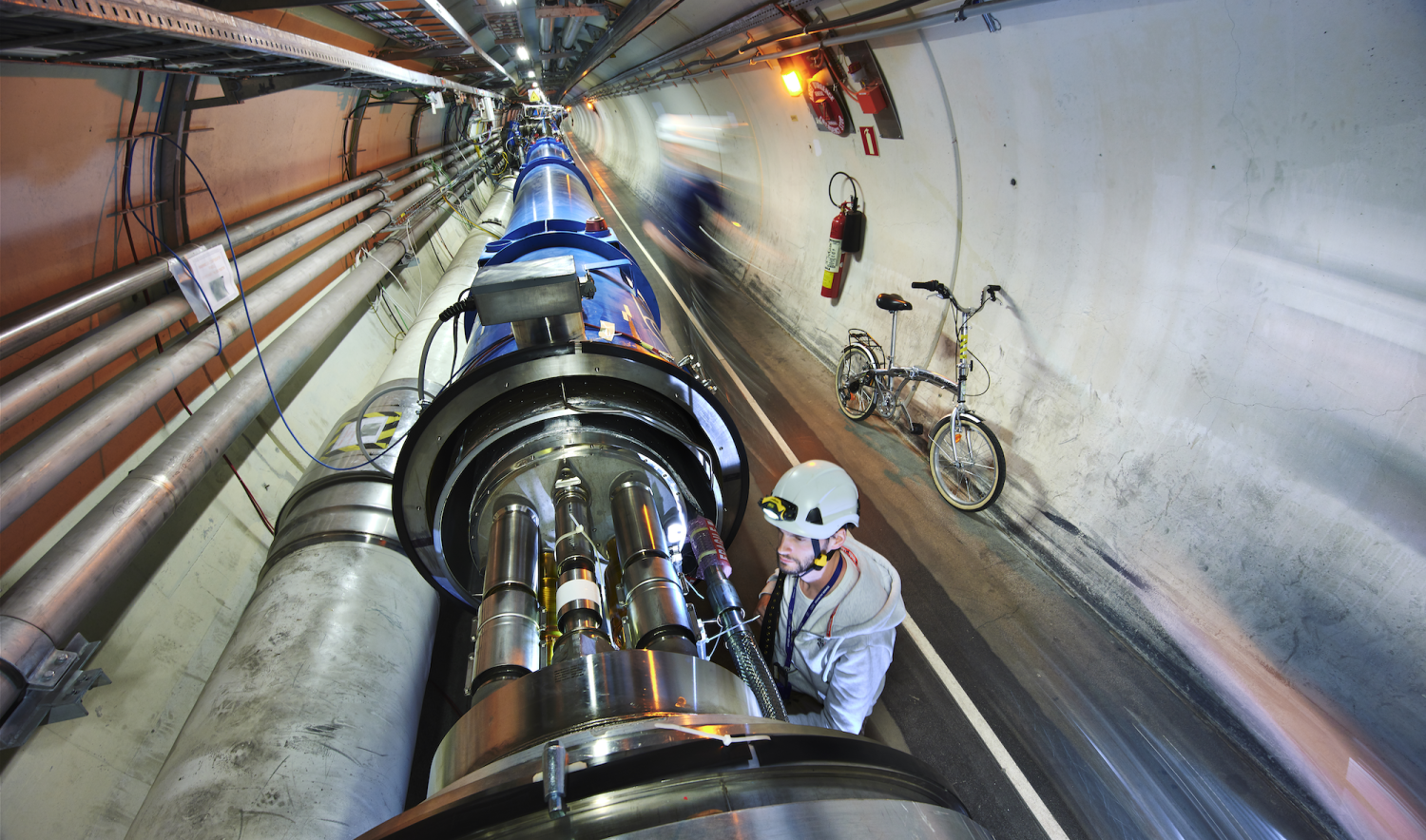 Man wearing hard hat works in a long tunnel with machinery running lengthwise