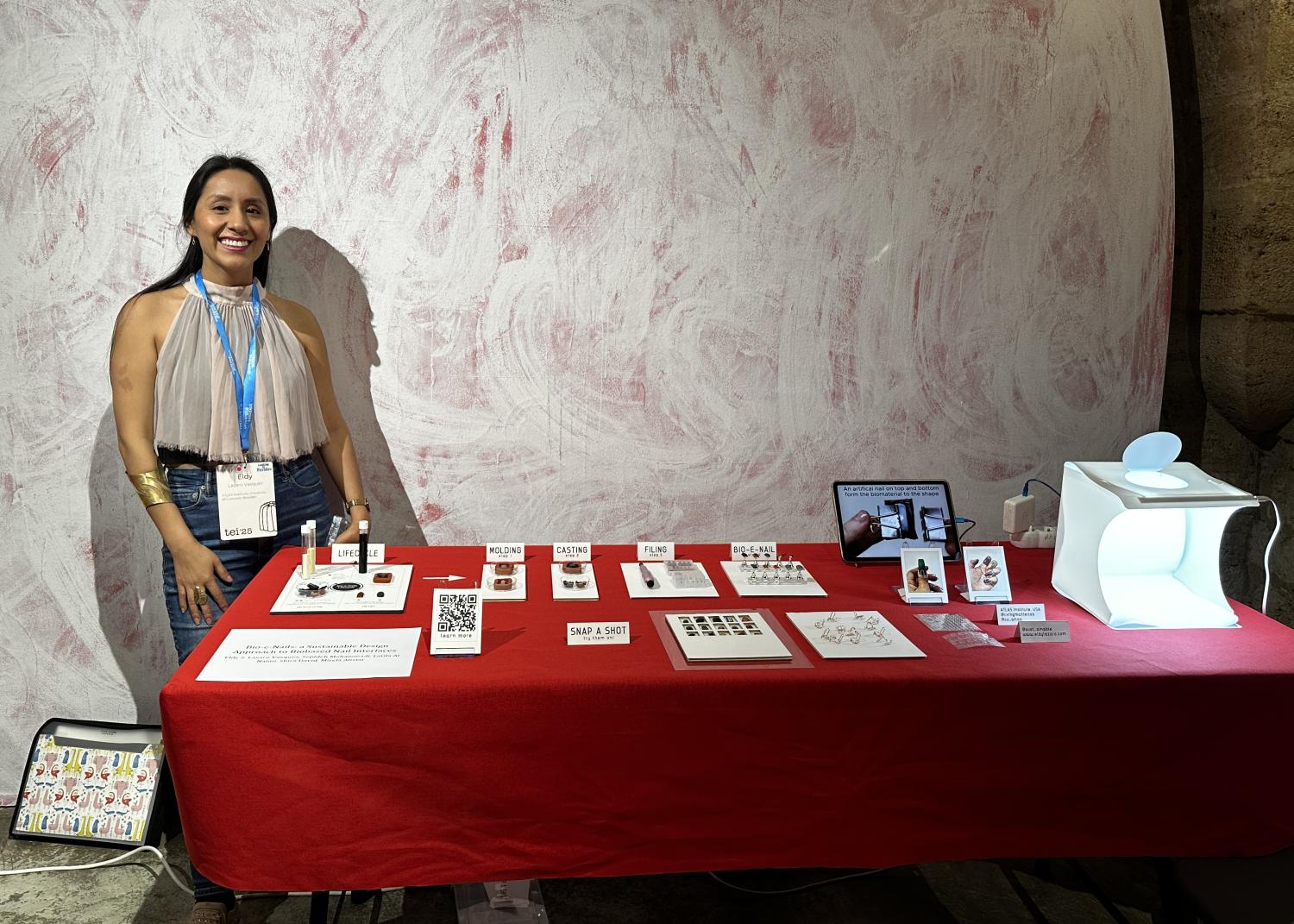 Woman stands in front of table with red tablecloth displaying multiple items