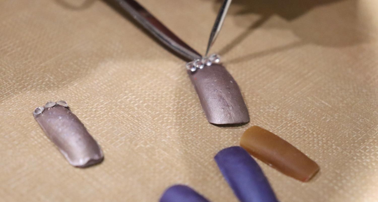 Tools place a crystal onto a press-on nail with more laying nearby