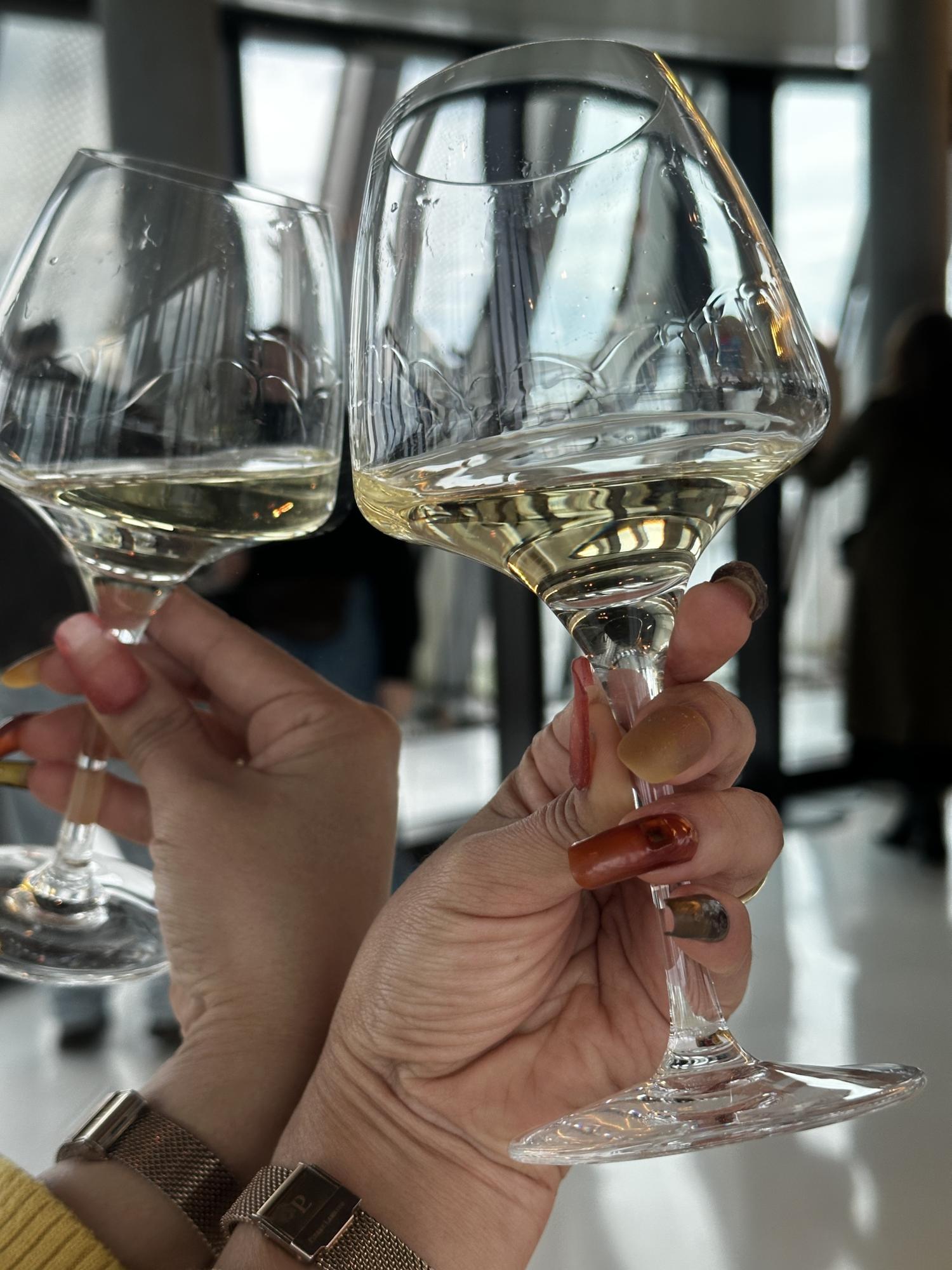 Hand with nails in several colors holds a wine glass against a mirror