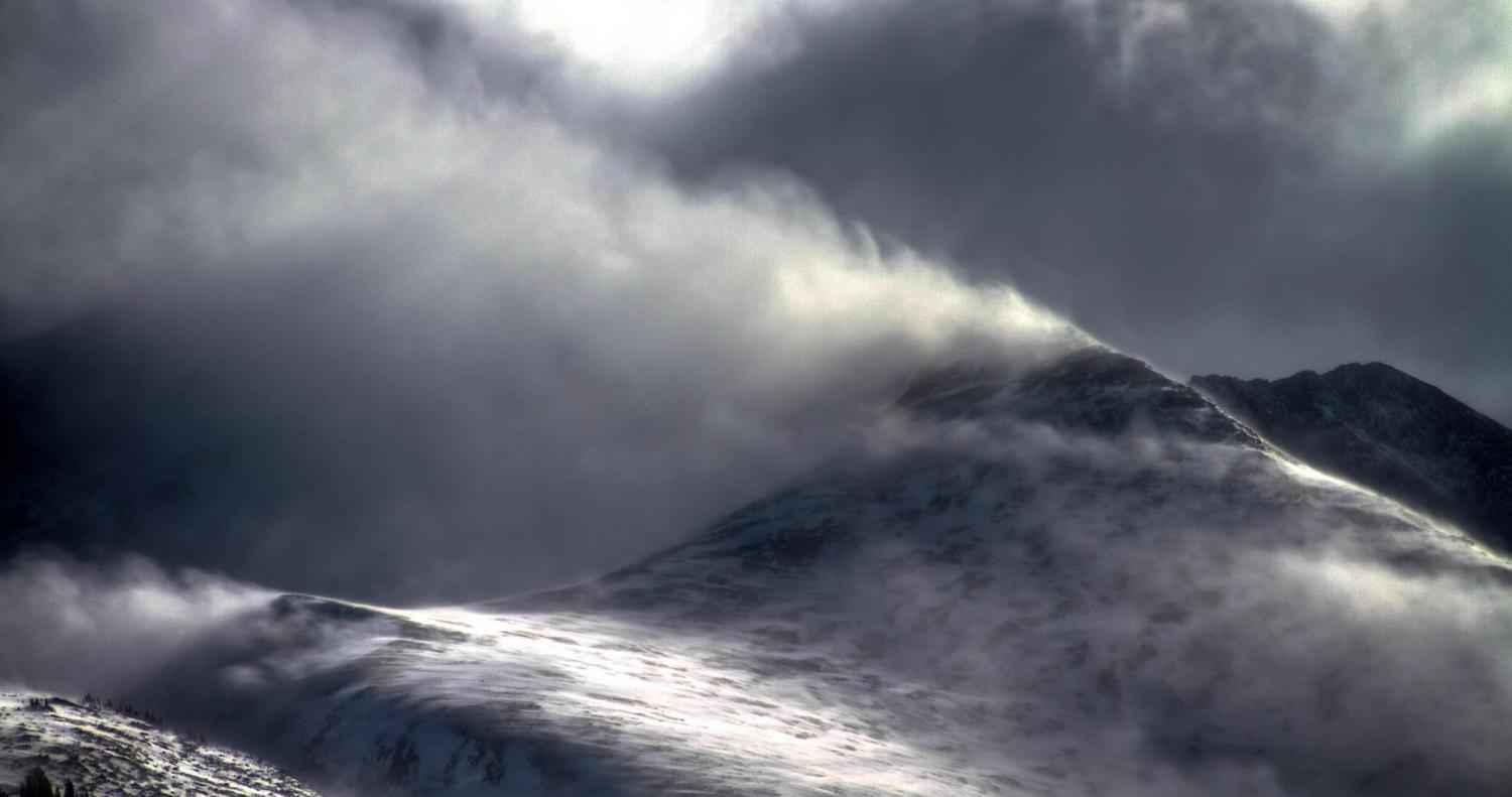 Snow flying off of a mountain top in the wind