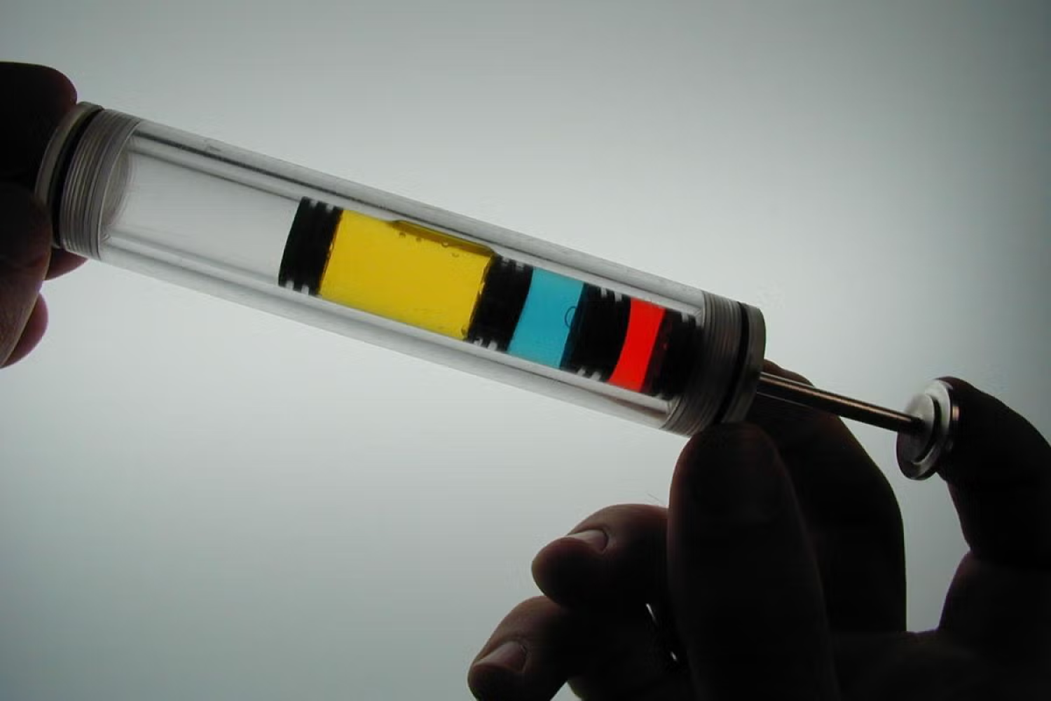 Hands hold clear tube filled with yellow, blue and red liquids