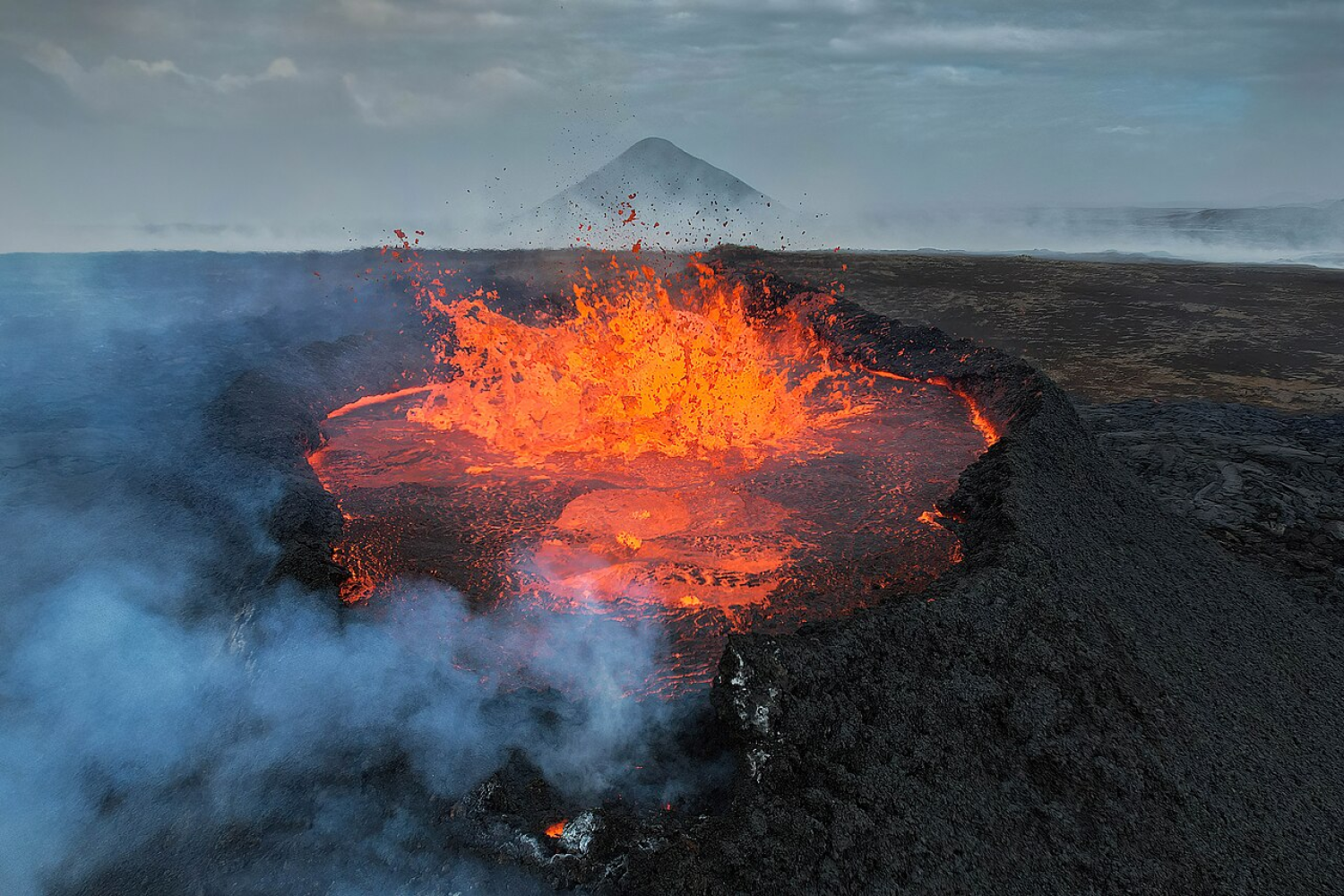 Photograph of volcano erupting with mountains seen in the background