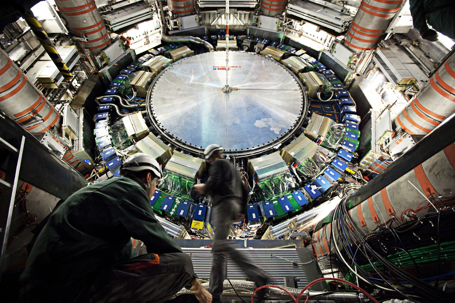 Two people walk in front of giant scientific device