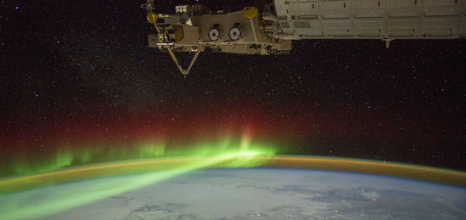 Spacecraft orbits above Earth, with an aurora shining in its atmosphere