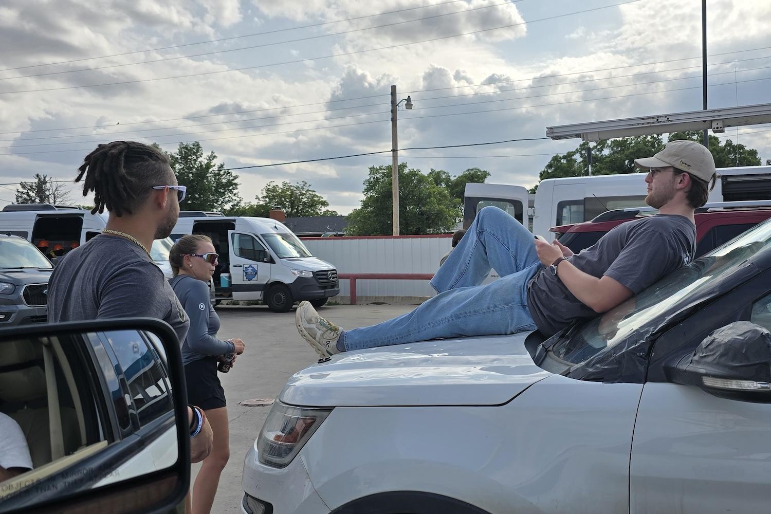 Man lies on hood of white sub and talks to two other people in front of car
