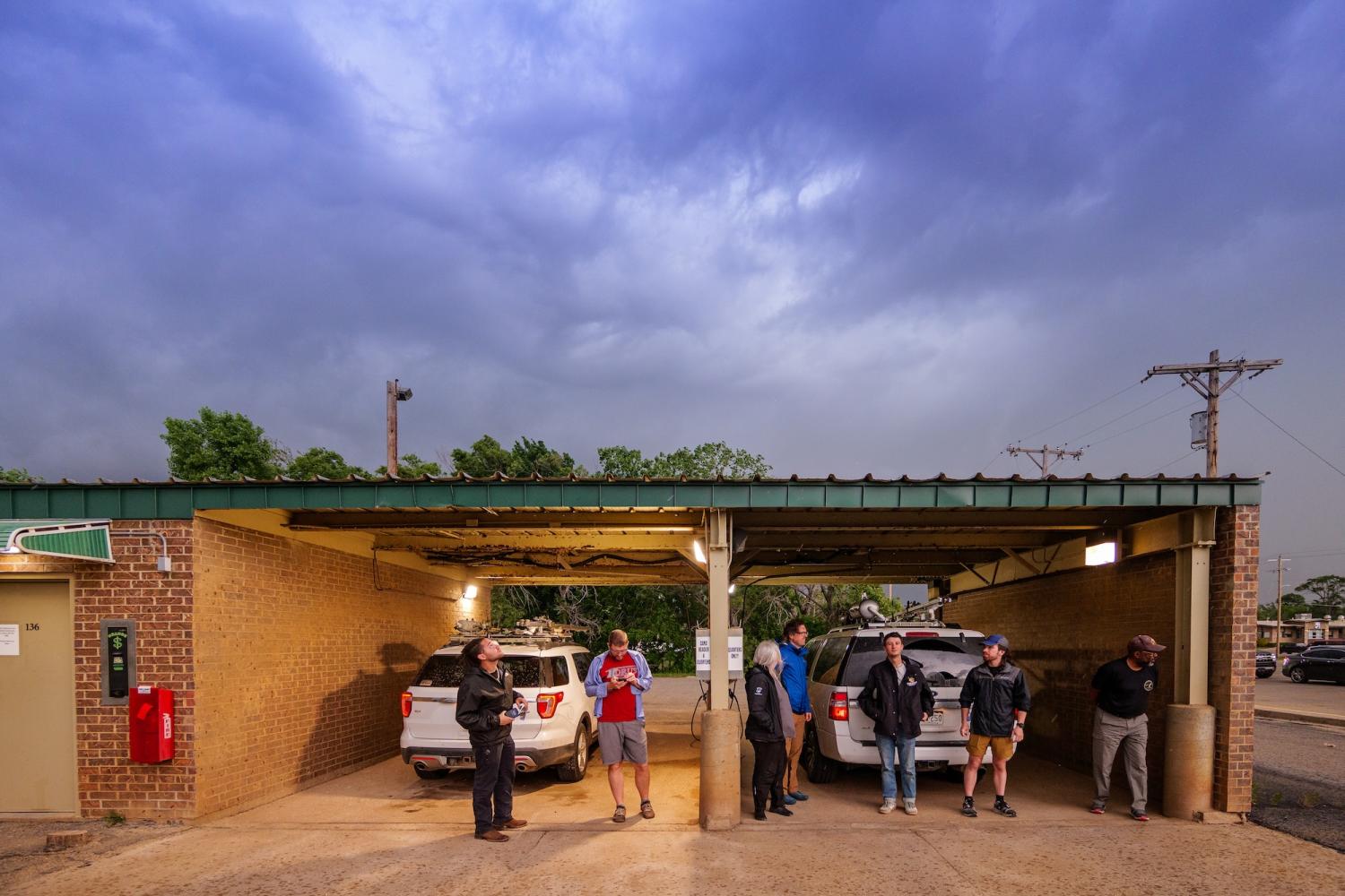 People stand in front of vehicles in the bay of a car wash as storm clouds loom overhead