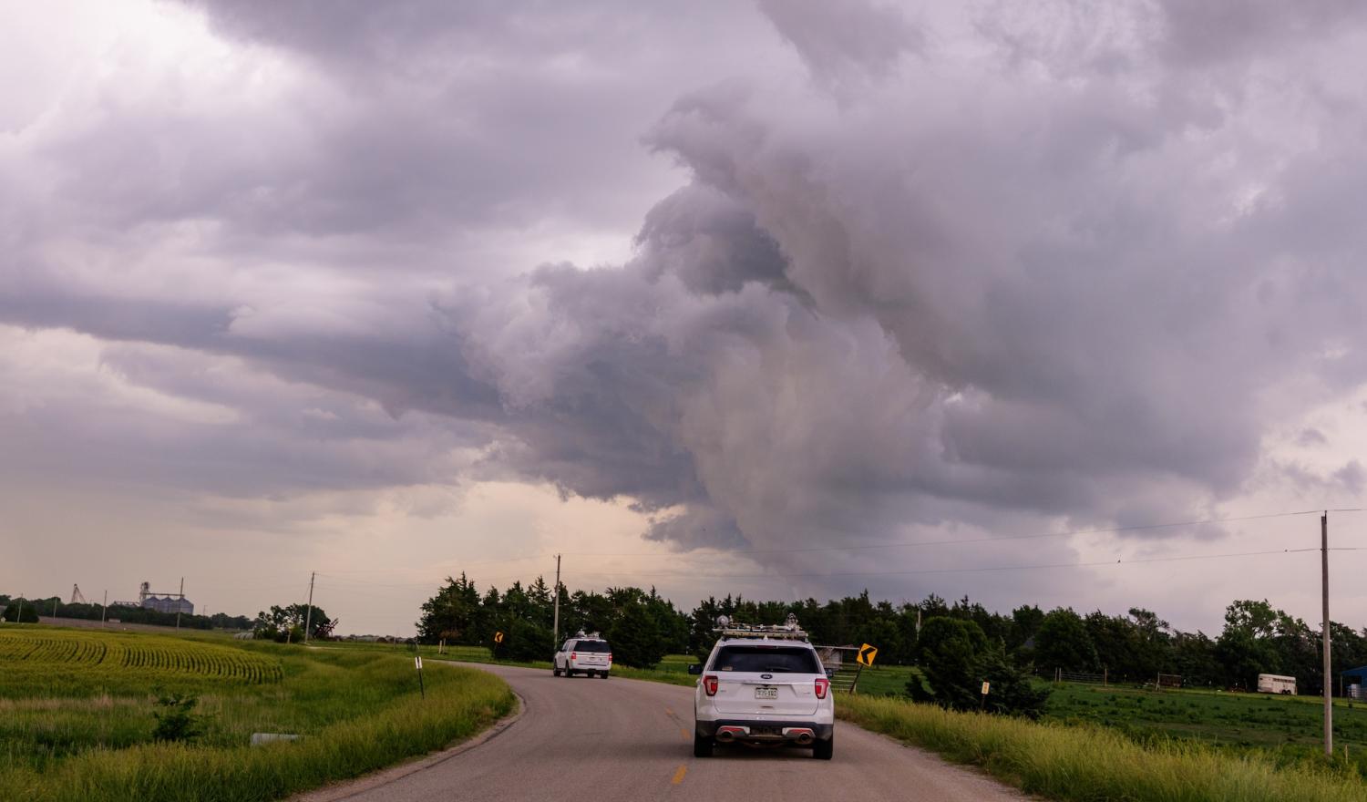 Two white SUVs drive down a single-lane highway in the country as gray storm clouds form overhead