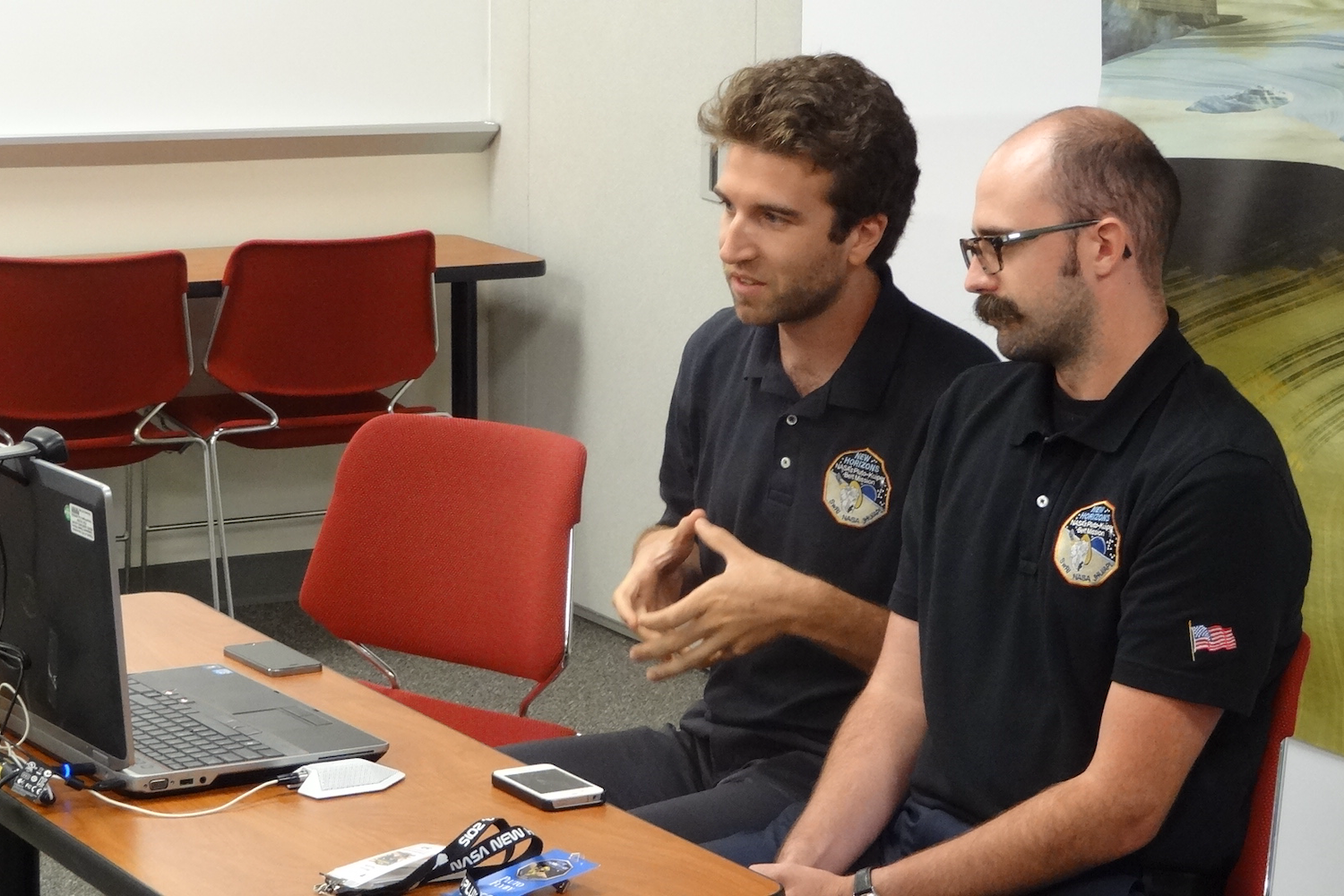 Two men in identical polo shirts look into a camera on a laptop